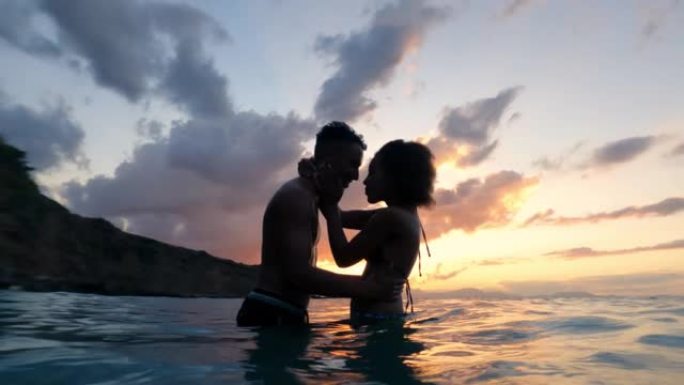 非洲民族浪漫爱情异性恋夫妇在金色日落时在海里游泳和拥抱