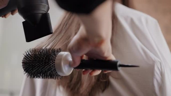 美发师的手用吹风机关闭，让顾客的头发拉直，在美发沙龙有亮点和切割新的头发外观后干燥。