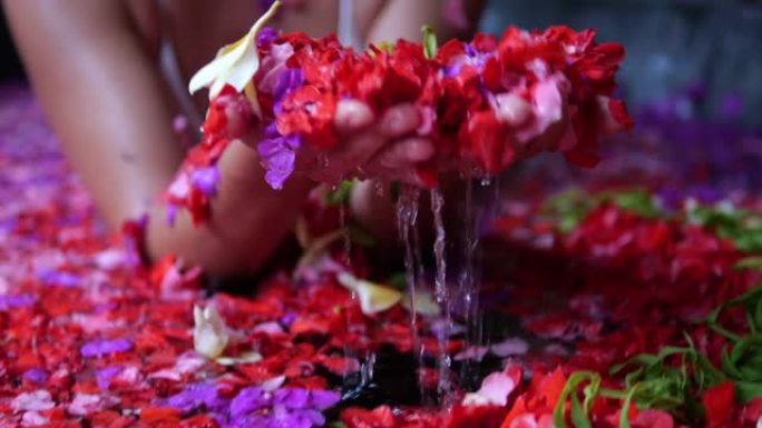一个女人在温泉旅馆里放松，浴缸里有红色和粉红色的花朵。鲜花芳香疗法概念。在巴厘岛的一家天堂酒店度假时