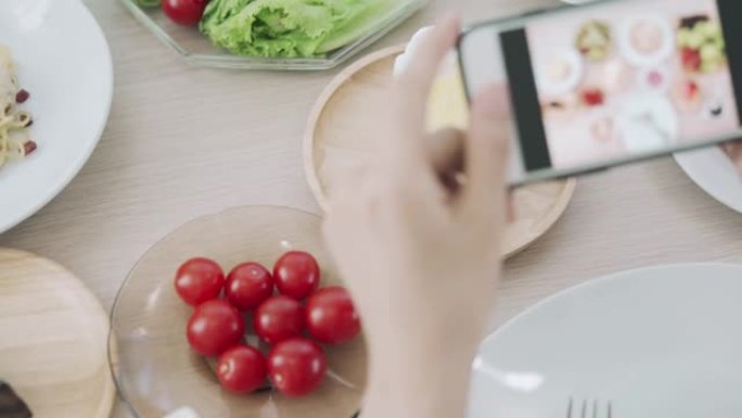 女性使用手机拍摄食物或在社交网络应用程序上拍摄实时视频。午餐的食物看起来很开胃。摄影和拍照以回顾食物