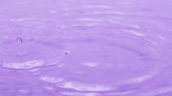 水滴落在水面上，在紫色背景上产生环