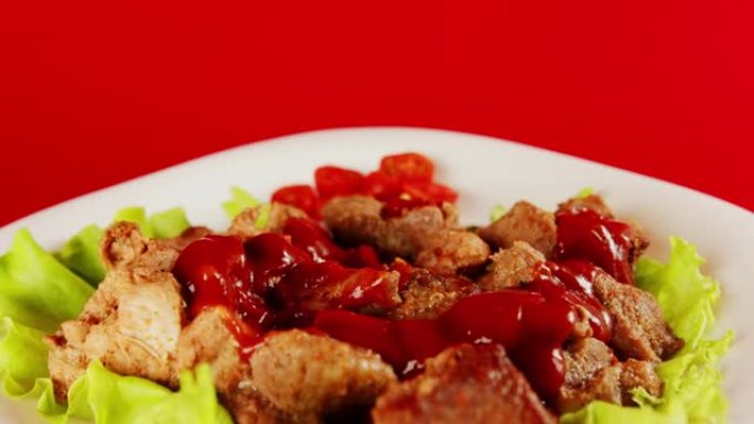 白盘莴苣上酱汁多汁的肉块。开胃调味的部分肉在红色背景上旋转的番茄酱。特写