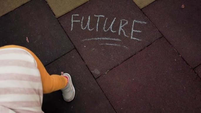 一个小女孩用粉笔在地上写下了 “未来” 的铭文。顶视图。更美好未来的概念