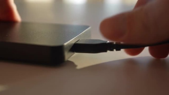 无法识别的人的极端特写手将USB电缆连接到桌子上的黑色外部硬盘驱动器，慢动作。