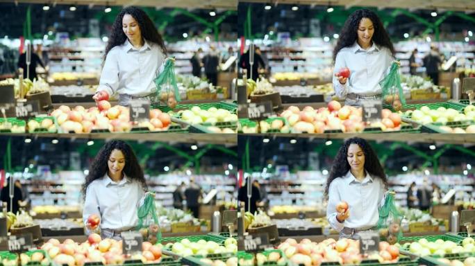 年轻漂亮的黑发女人在杂货店超市或市场的架子上选择和采摘水果，然后把它们放在生态袋里女顾客扔苹果
