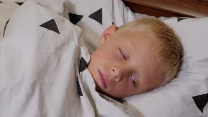 一个发烧的男孩正在家里的床上睡觉，他被毯子覆盖着。