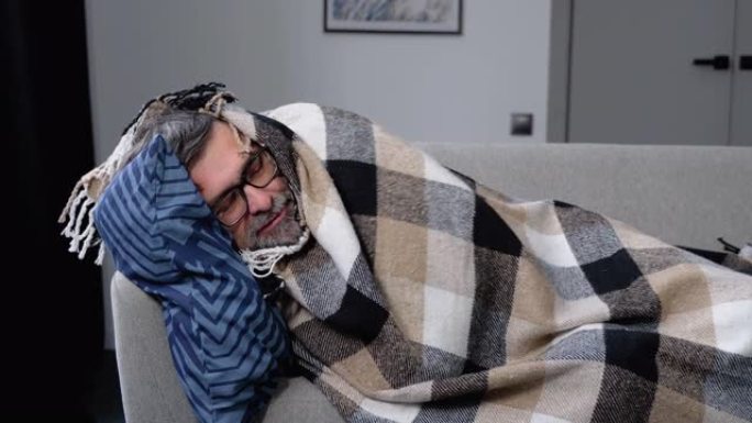 患有流感，发烧和头痛的生病的老人躺在沙发上的格子里。季节性疾病时期。病毒性疾病的概念
