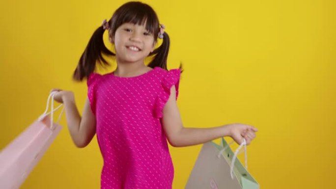 黄色背景上拿着购物袋的小女孩。