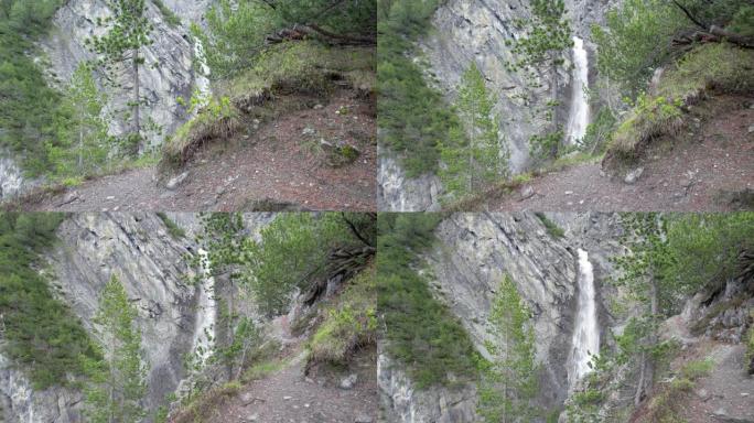 空中无人机向左缓慢滚动，揭示了一个戏剧性的瀑布，瀑布层叠在瑞士被松树包围的陡峭山崖边缘。