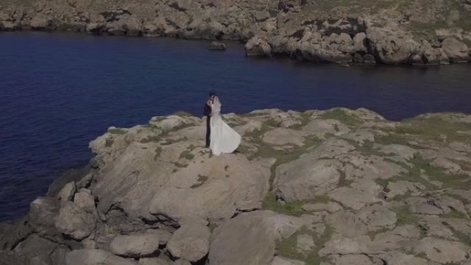 穿着婚纱的新娘和新郎沿着海边散步，拥抱，亲吻，奔跑，享受自己。鸟瞰的航空摄影。夫妻正在度假的酒店拍摄