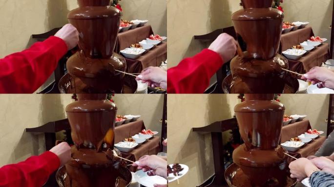 酒店餐厅的巧克力火锅。木串上的水果被巧克力覆盖。把手放在框架里。