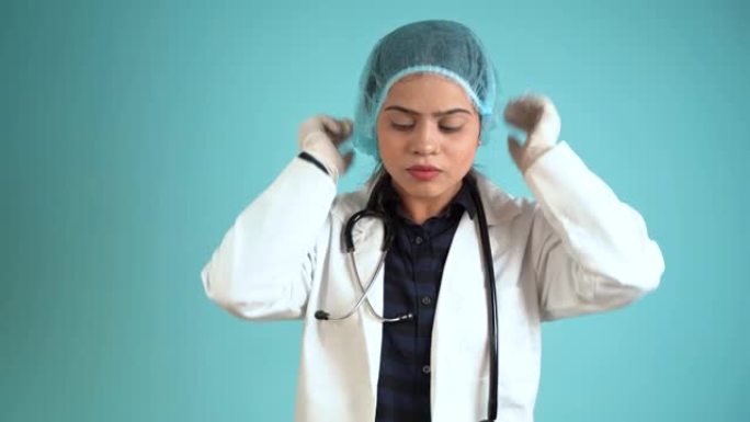 一位年轻的女医生戴着头套的肖像，穿着围裙的亚洲印度女医生和听诊器被隔离在蓝色工作室背景上