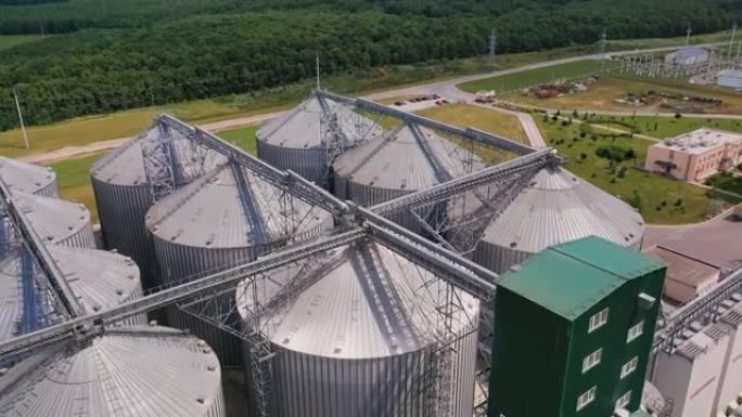 用于农业收获的大型钢库。在巨大的筒仓储罐复合体上空飞行。背景是美丽的绿色植物。