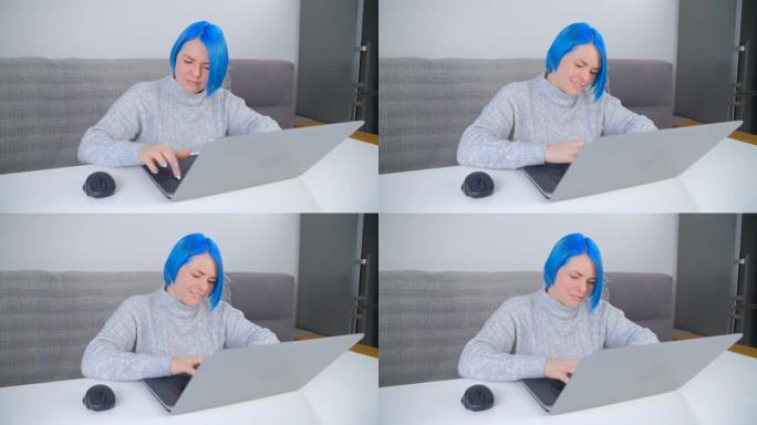 快乐的千禧女性在电脑上打字。时尚的白人女性，染成蓝色头发，远离家乡工作。美丽的高加索人在笔记本电脑上