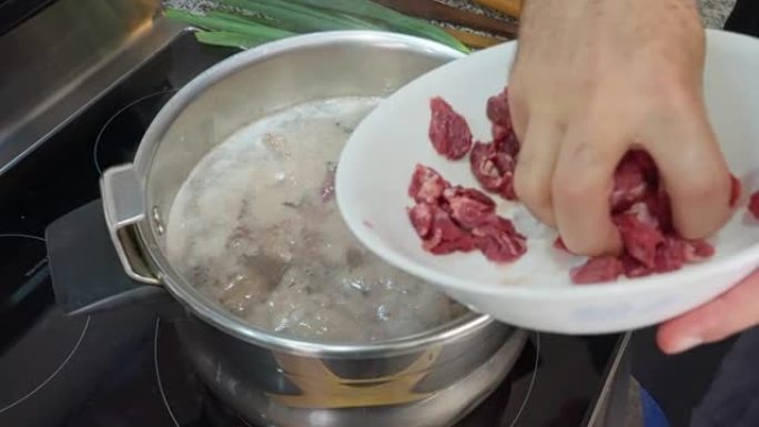 西班牙裔男子将切碎的猪肉放入沸水中。