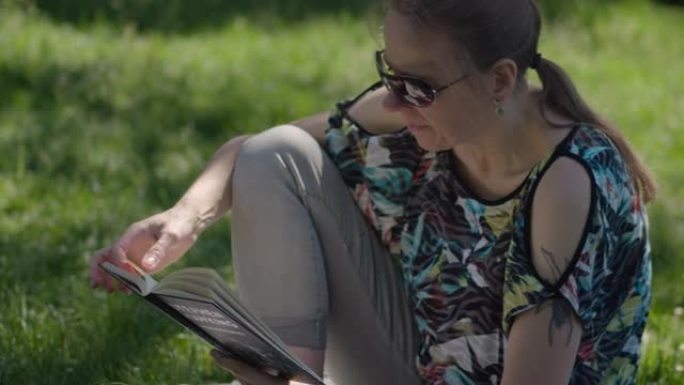 戴着墨镜的女人坐在公园里放松的草地上看书