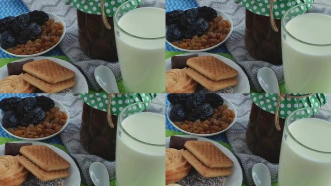 在桌子上的彩色餐巾纸，一杯牛奶，一罐果酱，一茶匙，两个带有葡萄干，李子，饼干和糖果的碟子。早餐产品的