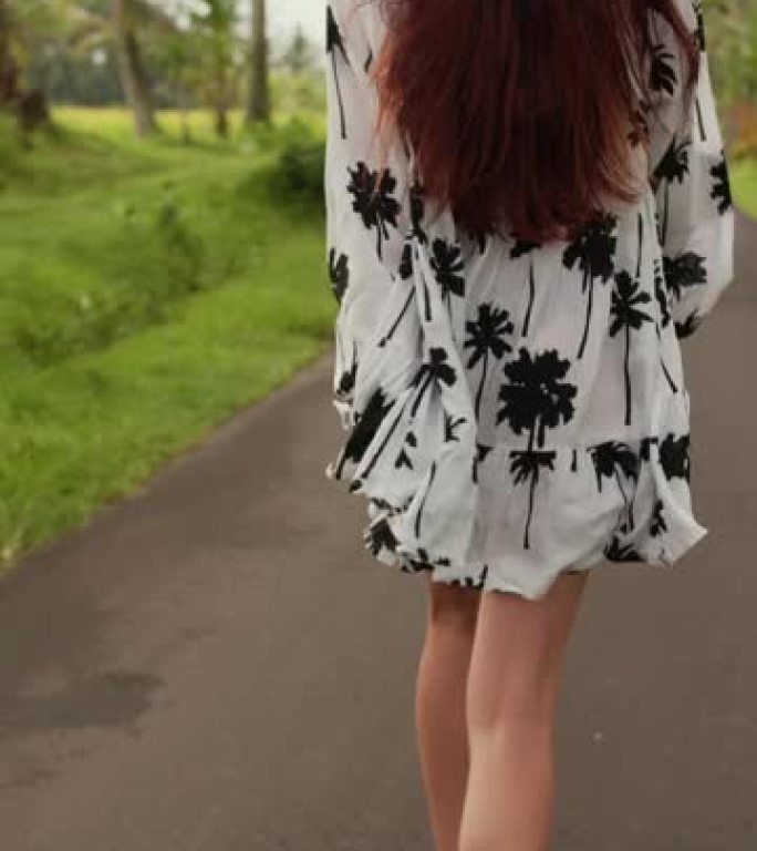 垂直视频一个穿着裙子的年轻女孩在棕榈树间奔跑