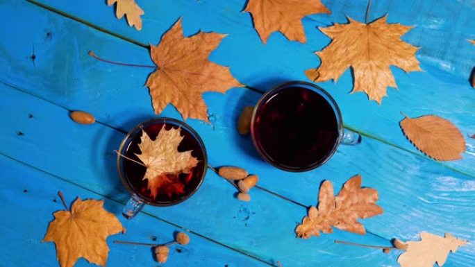 慢动作秋季背景顶视图，茶杯上有黄色叶子的老式木桌。美丽的背景，有树叶和一杯茶。
