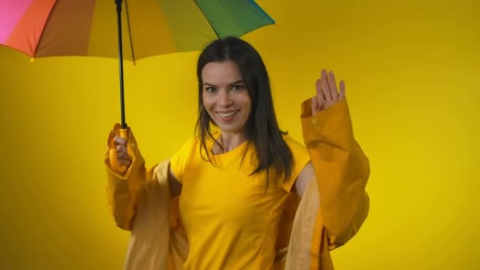 穿着黄色雨衣的快乐迷人女人站在彩虹伞下