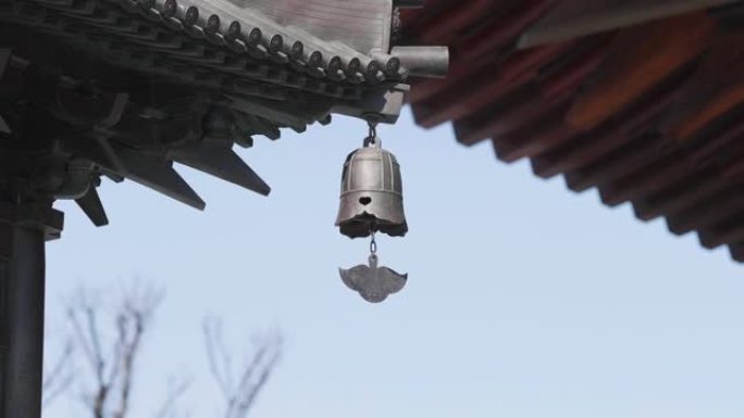 近距离的青铜钟摇摆在风与寺庙建筑的背景，4k慢动作镜头。