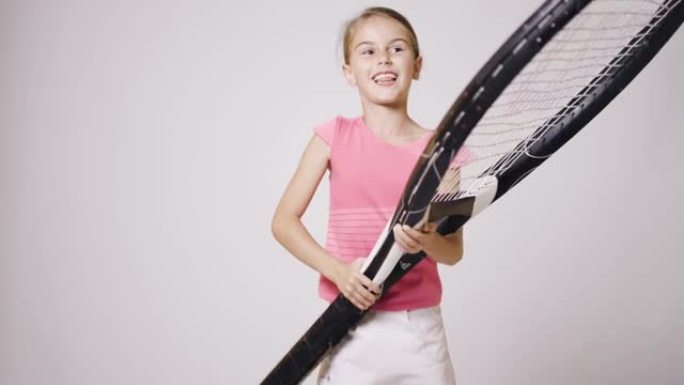 年轻的女子网球运动员手里拿着超大球拍。穿着粉色运动服跳跃的快乐微笑女孩。