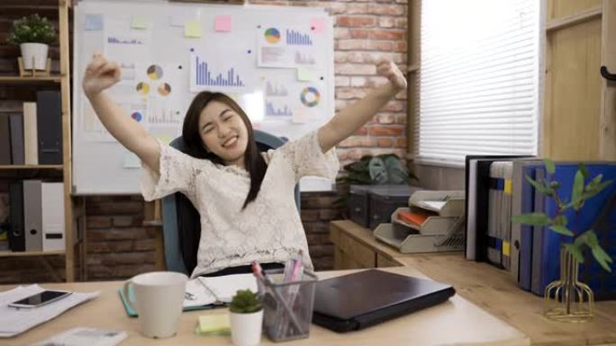 亚洲女性创意工作者关闭笔记本电脑正在锻炼她的颈部肌肉，伸展身体，对在办公室完成工作感到高兴。