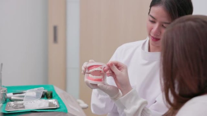 一名年轻女性患者正在接受一名亚洲女医生的治疗。讨论了治疗计划。在模型上，一名穿着医疗服的牙医女士显示