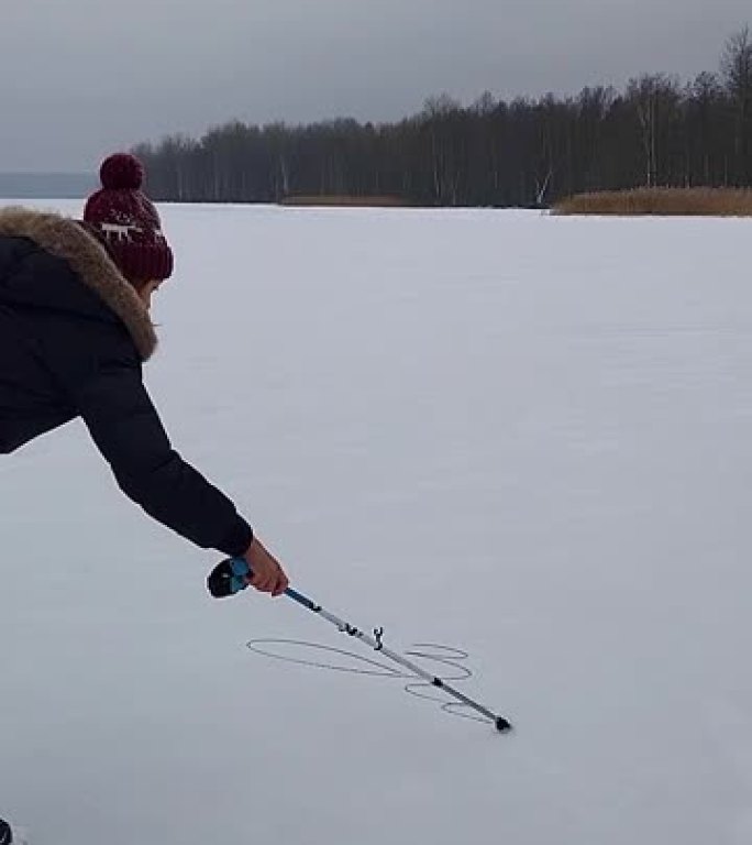 女人在雪地里用滑雪杖写冬天。寒冷的冬日，森林湖上刚下的雪
