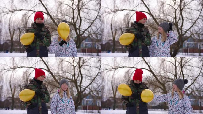 正面视图欢快的少年男孩和女孩拿着黄色气球对着脸开口大笑。快乐无忧无虑的高加索朋友在多云的冬季公园慢动