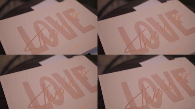 可爱的爱情铭文写在粉红色的纸上。粉色字母，这是写在婚礼相册上的爱情，慢动作镜头。