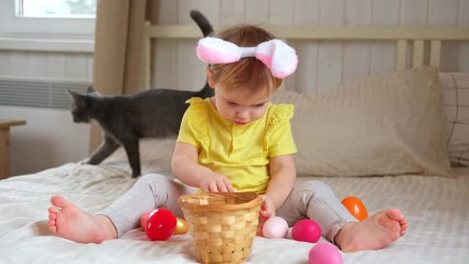 有兔子耳朵的女婴。可爱的搞笑宝宝在家玩复活节彩蛋。孩子在室内玩五颜六色的鸡蛋。春。用节日和宗教概念的