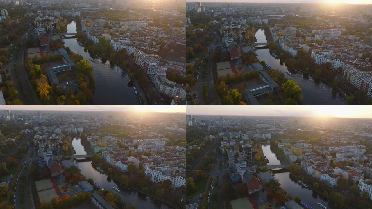 日落时，在城市的河边向前飞。船在平静的水面上航行，岸边被秋天的彩树包围。德国柏林