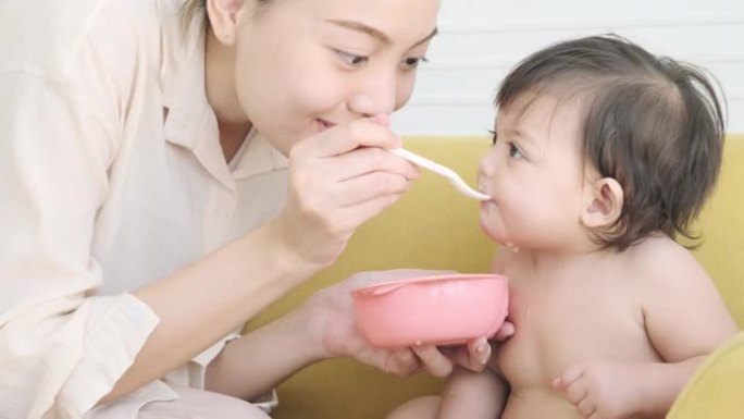 年轻的母亲用勺子喂她的小女儿吃食物。