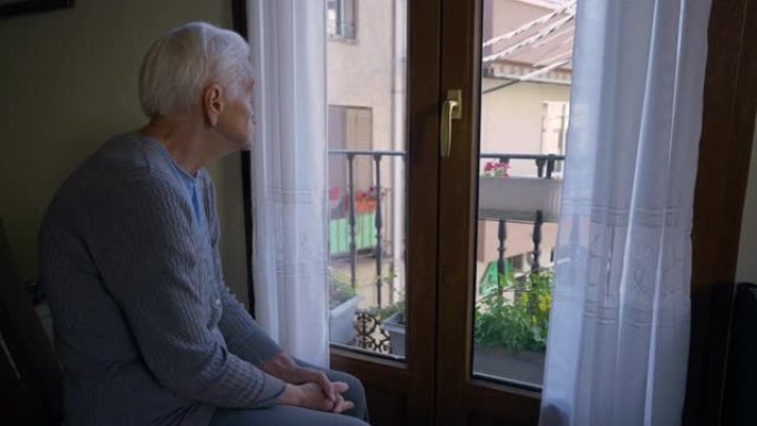 悲伤孤独的老妇人看着窗外，坐在室内左边。白发白人女性退休人员想着夏天在家休息。生活方式和衰老概念。