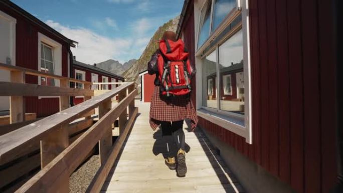美丽的年轻女孩旅行者去传统红色rorbu前往挪威罗弗登的背景下的木制码头