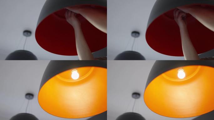 专业的手更换灯泡挂灯和照亮它与一个温暖的红色辉光。