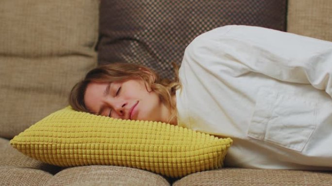 疲惫的年轻女子躺在家里沙发上的枕头上睡觉。女孩感到筋疲力尽，精力不足，不知所措