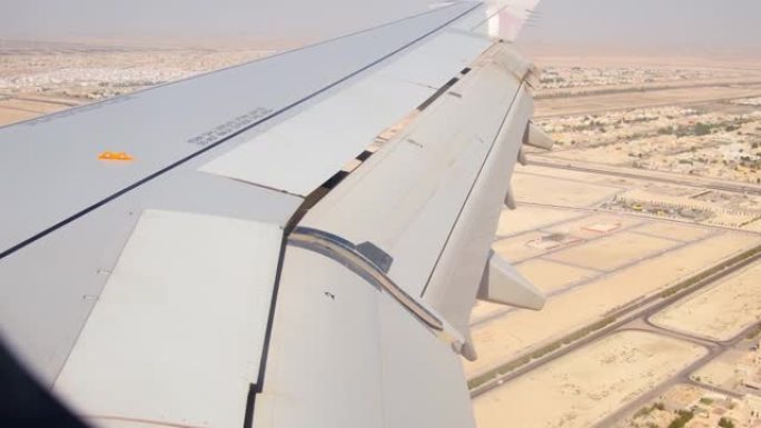 阿布扎比市郊区和沙漠的鸟瞰图，带有翅膀背景窗口。阿联酋荒芜的风景和机舱的飞机机翼景观。中东概念中的假