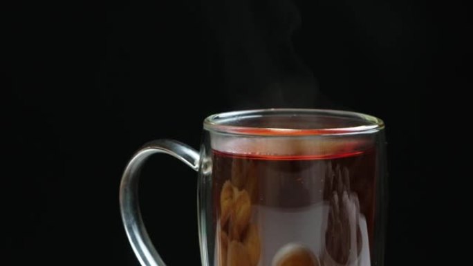 在黑色背景上有双层底蒸的玻璃杯中的热红茶。