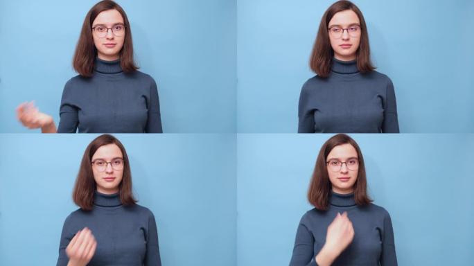 一个戴着眼镜和毛衣的学生女孩的肖像，挥舞着她的手，邀请她在4K的蓝色背景上站起来。过来。非语言交流