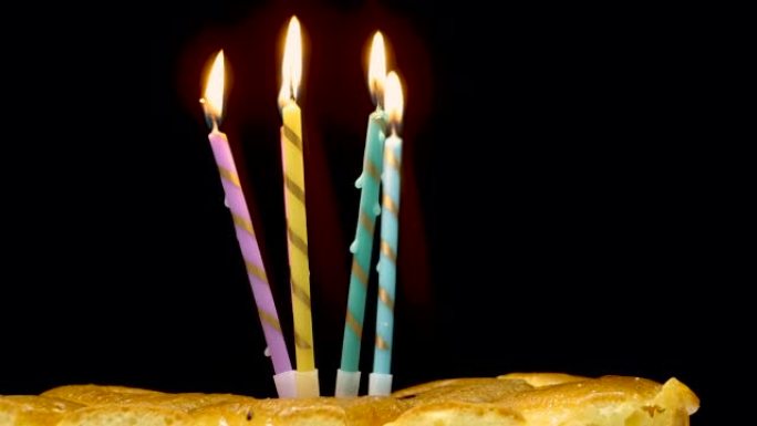 黑色背景蛋糕上多色燃烧蜡烛的特写镜头。燃烧蜡烛的生日快乐背景。