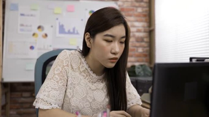 韩国女创意工作者正在点头，意识到按摩的意义，同时支撑着脸，在办公桌上沉思地看着笔记本电脑屏幕。