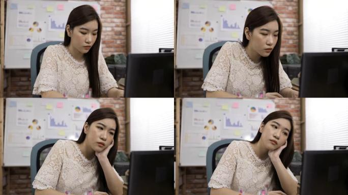 韩国女创意工作者正在点头，意识到按摩的意义，同时支撑着脸，在办公桌上沉思地看着笔记本电脑屏幕。