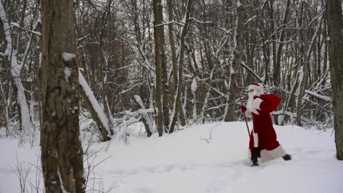 圣诞老人带着魔法杖和一袋圣诞礼物走在雪林里。