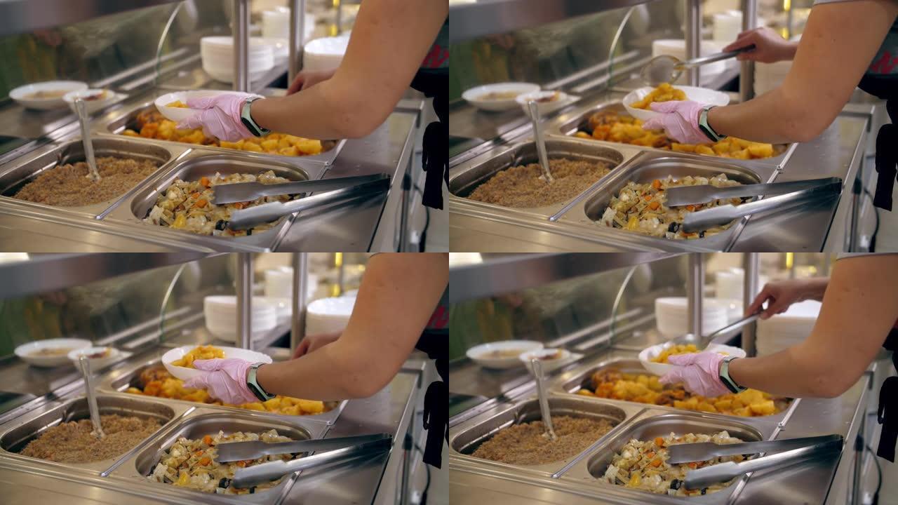 自助餐厅。自助餐厅。特写镜头。女服务员戴着防护手套，为顾客把食物放在盘子里。烹饪。健康食品