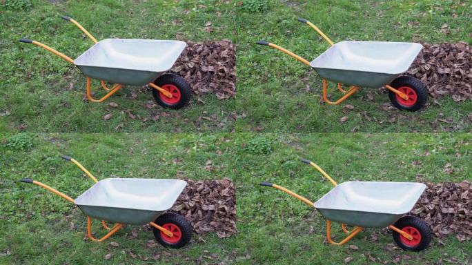 橙色花园独轮车靠近一堆干燥的落叶。秋季的最后工作-在花园里清洁干燥的叶子。在季节性清洁期间，空的钢制