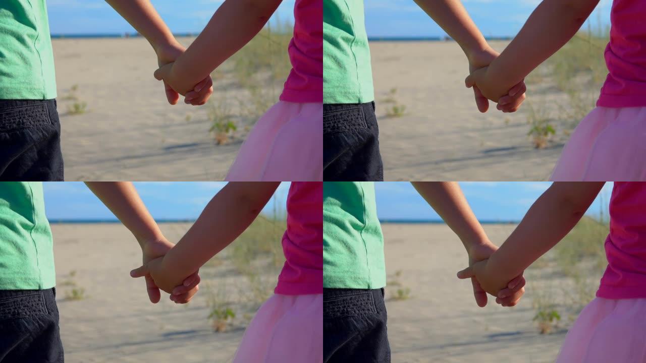 穿着粉红色裙子的小男孩和女孩在海滩上牵手的特写