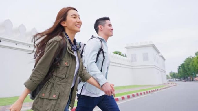 亚洲迷人的浪漫情侣在城市旅行度蜜月。年轻的新婚男女背包客游客牵着手过马路，一起享受度假时光