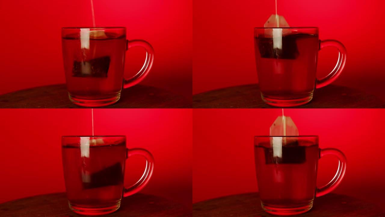 红色背景上的透明红茶杯。面目全非的人把茶包浸在杯子里。快速酿造和茶点的概念